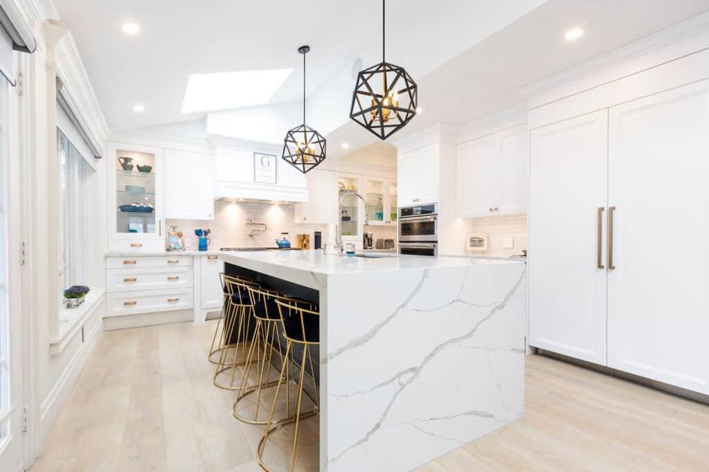 A modern white kitchen with waterfall edge veined quartz countertops.