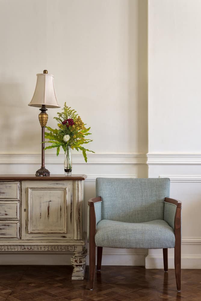 Creamy white walls with buffet and blue chair.