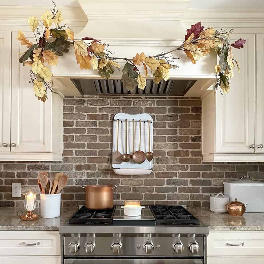 A kitchen with a brick wall and fall garland over stove.